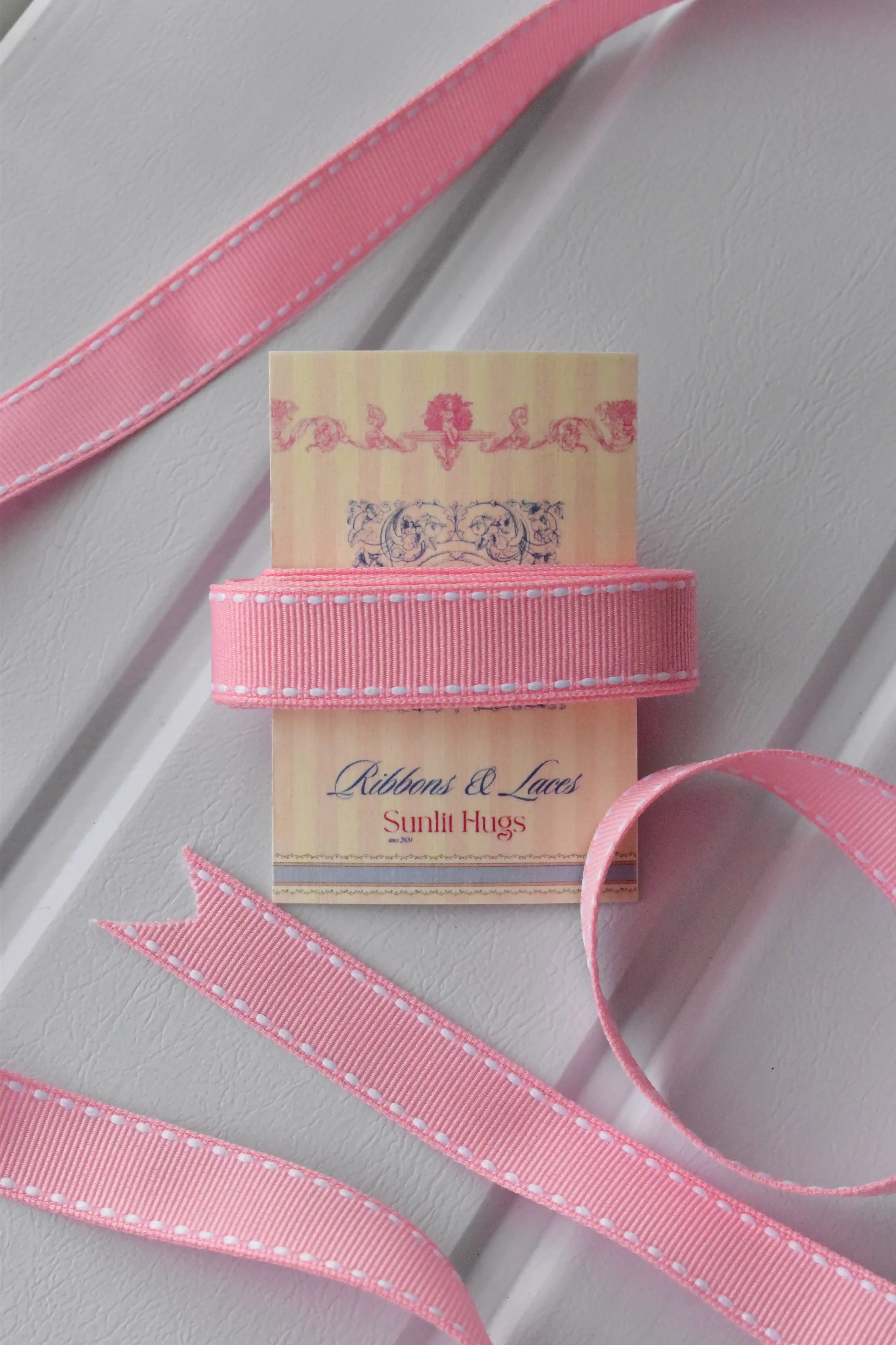 A red ribbon with white stitching is wrapped around a "Sunlit Hugs" tag.