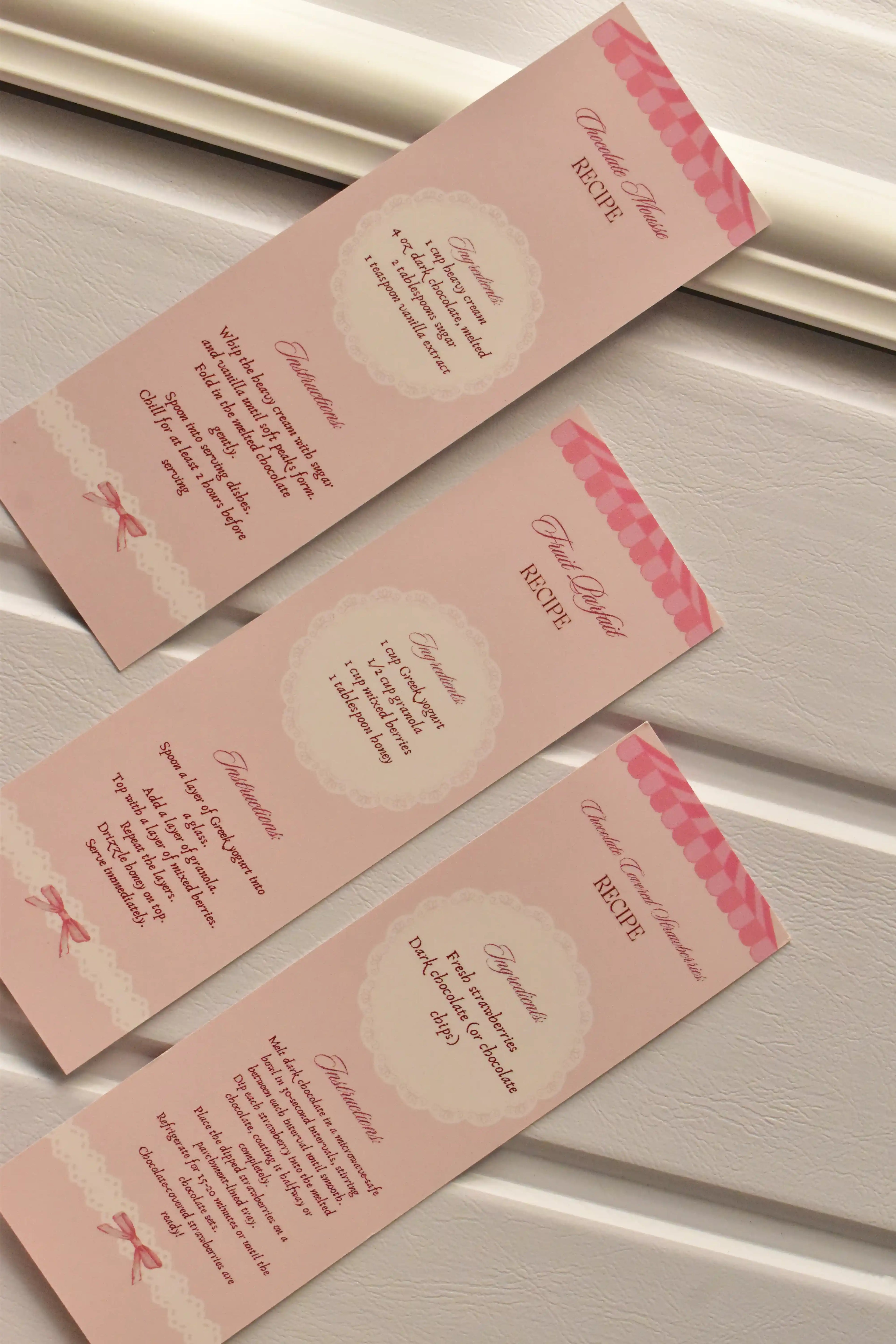 A comprehensive view showing the back side of all three pastel pink bookmarks, detailing the three unique dessert recipes included in the set.