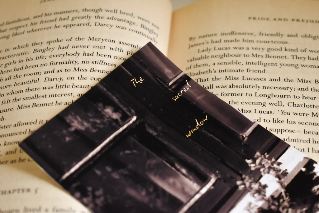 Angled close-up of the 'The Sacred Window' Landour Photo Print by Anneshwa Paul placed on the pages of a classic novel, highlighting the dark academia aesthetic and elegant golden typography.