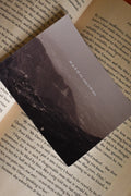 Angled view of the 'Ek Tum Hi Nahi Tanha' Landour Photo Print tucked inside a vintage book, highlighting the moody, high-contrast mountain shadows and delicate Hindi typography.