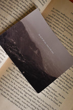 Angled view of the 'Ek Tum Hi Nahi Tanha' Landour Photo Print tucked inside a vintage book, highlighting the moody, high-contrast mountain shadows and delicate Hindi typography.