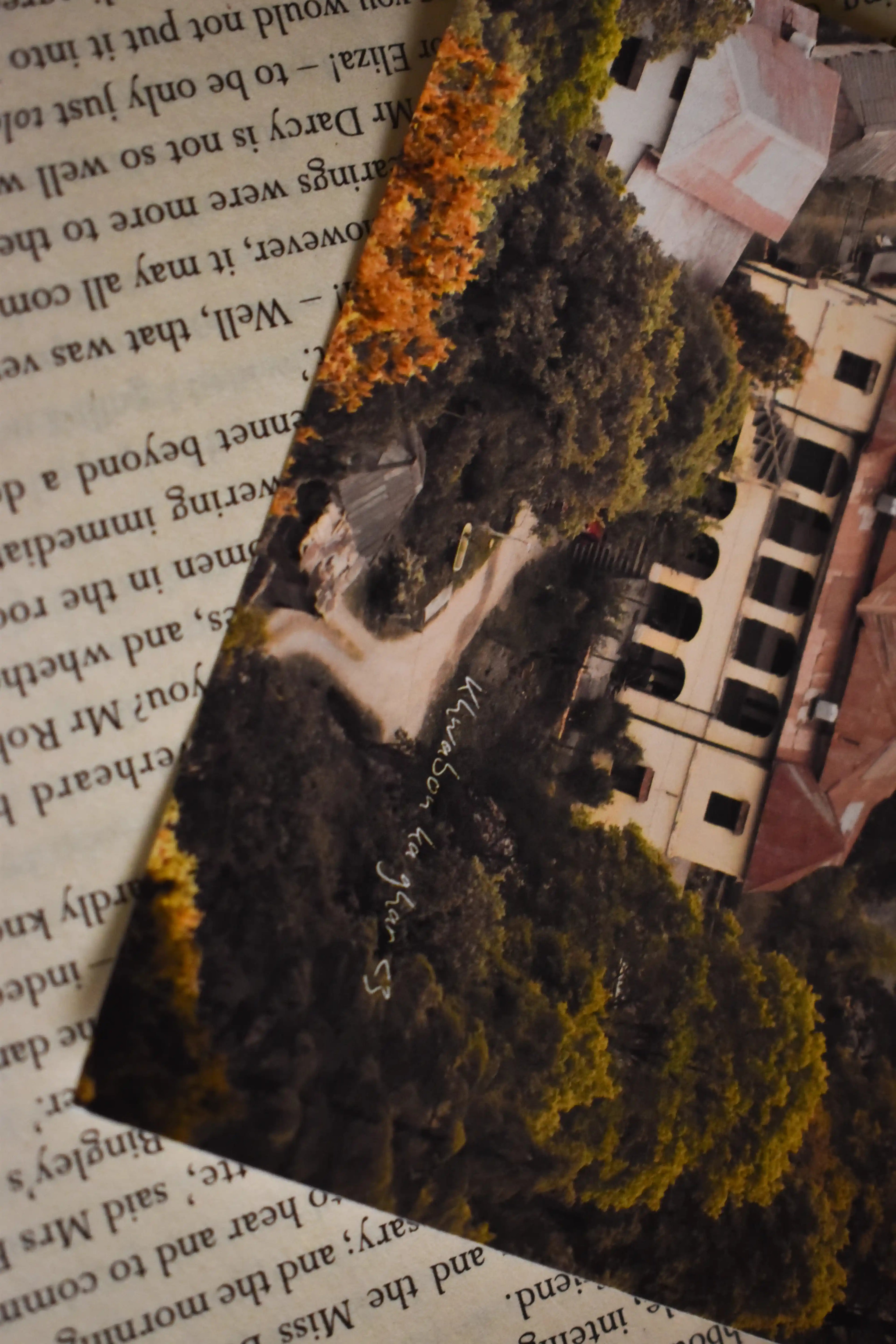 Angled close-up of the 'Khwabon Ka Ghar' Barlowganj Photo Print resting on the text-filled pages of a vintage book, highlighting the colonial estate and handwritten text overlay.