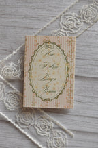 Angled flat lay of the Sunlit Hugs How I Love Being a Woman Greeting Card showing the vintage pink striped and floral design resting beside decorative white lace.