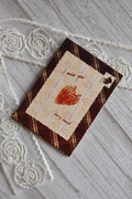 Angled flat lay of the Sunlit Hugs I Miss You Berry Much Greeting Card showing the brown plaid pattern, lace graphic, and strawberry design next to white lace.