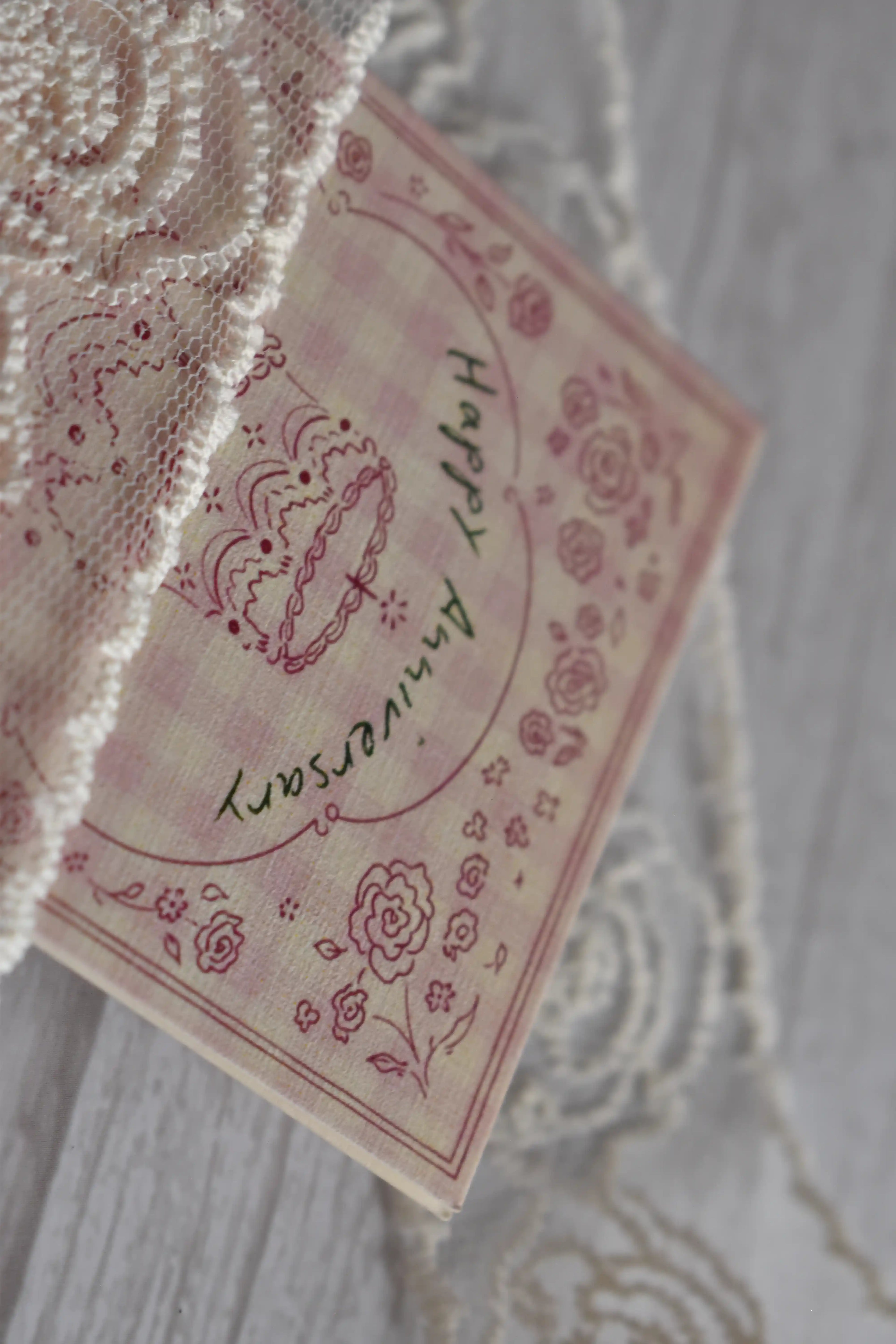 Angled view of the Sunlit Hugs Happy Anniversary Vintage Cake Greeting Card displayed over a pink envelope with white lace detailing.
