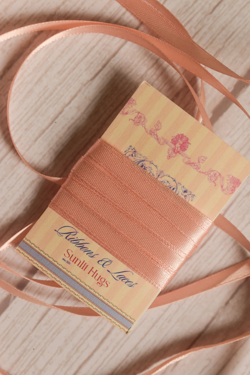 Apricot Satin Ribbon shown with loose satin strands around the product card, highlighting its slim 6 mm width, peach-toned warmth, and soft shine for crafts and gift wrapping.