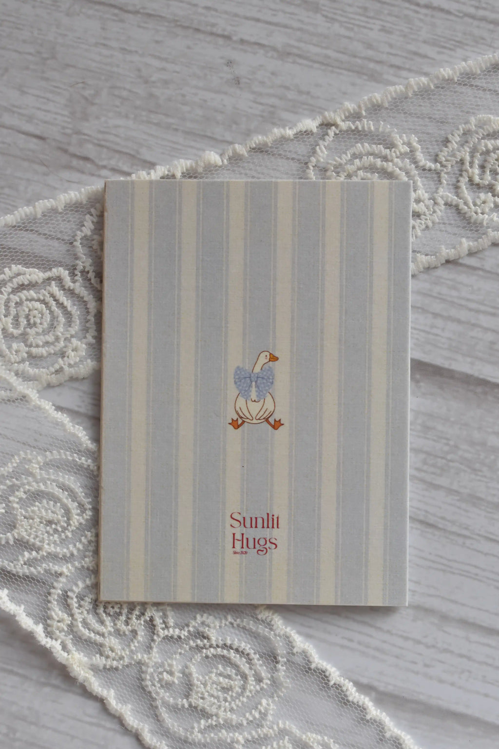 Back cover of the Sunlit Hugs Get Well Soon Cozy Soul Greeting Card featuring a cute goose with a blue bow tie on a striped background.