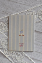 Back cover of the Sunlit Hugs Get Well Soon Cozy Soul Greeting Card featuring a cute goose with a blue bow tie on a striped background.