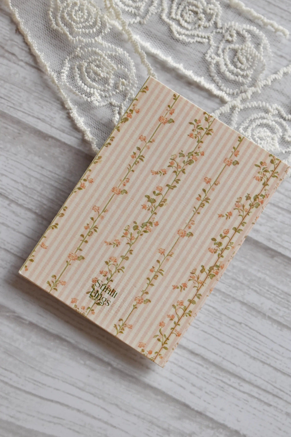 Back cover of the Sunlit Hugs How I Love Being a Woman Greeting Card featuring pink stripes, delicate floral vines, and the Sunlit Hugs logo.