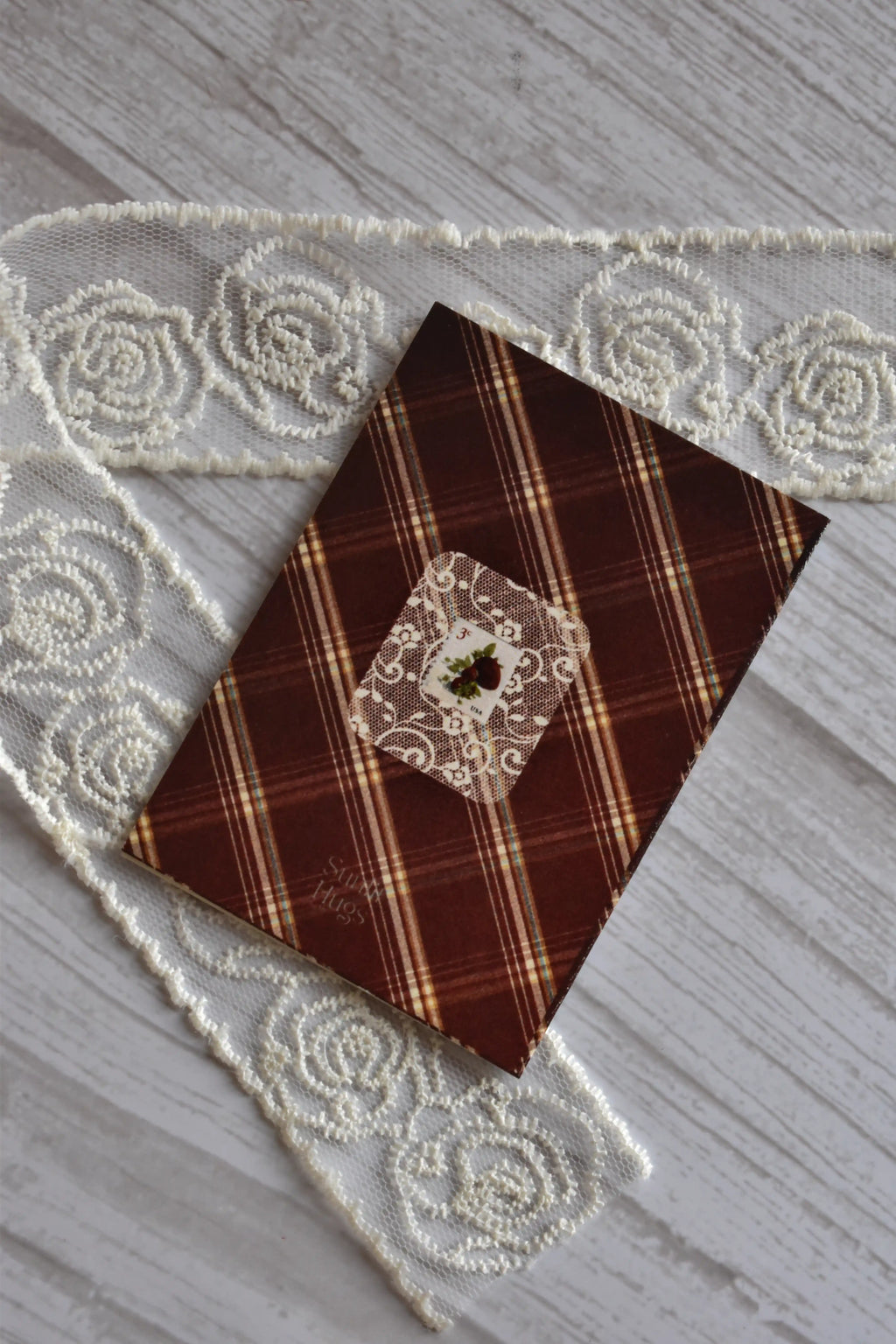 Back cover of the Sunlit Hugs I Miss You Berry Much Greeting Card featuring a brown plaid pattern, a faux stamp on a lace square, and the brand logo.