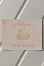 A close-up of the front of the Birthday Tea Postcard, highlighting the delicate pink striped background and the whimsical teacup illustration, ready to send a warm, personal invitation.
