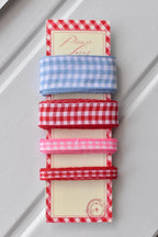 Four gingham ribbons—wide light blue, wide red, narrow pink, and narrow red—displayed vertically on a themed ribbon card.