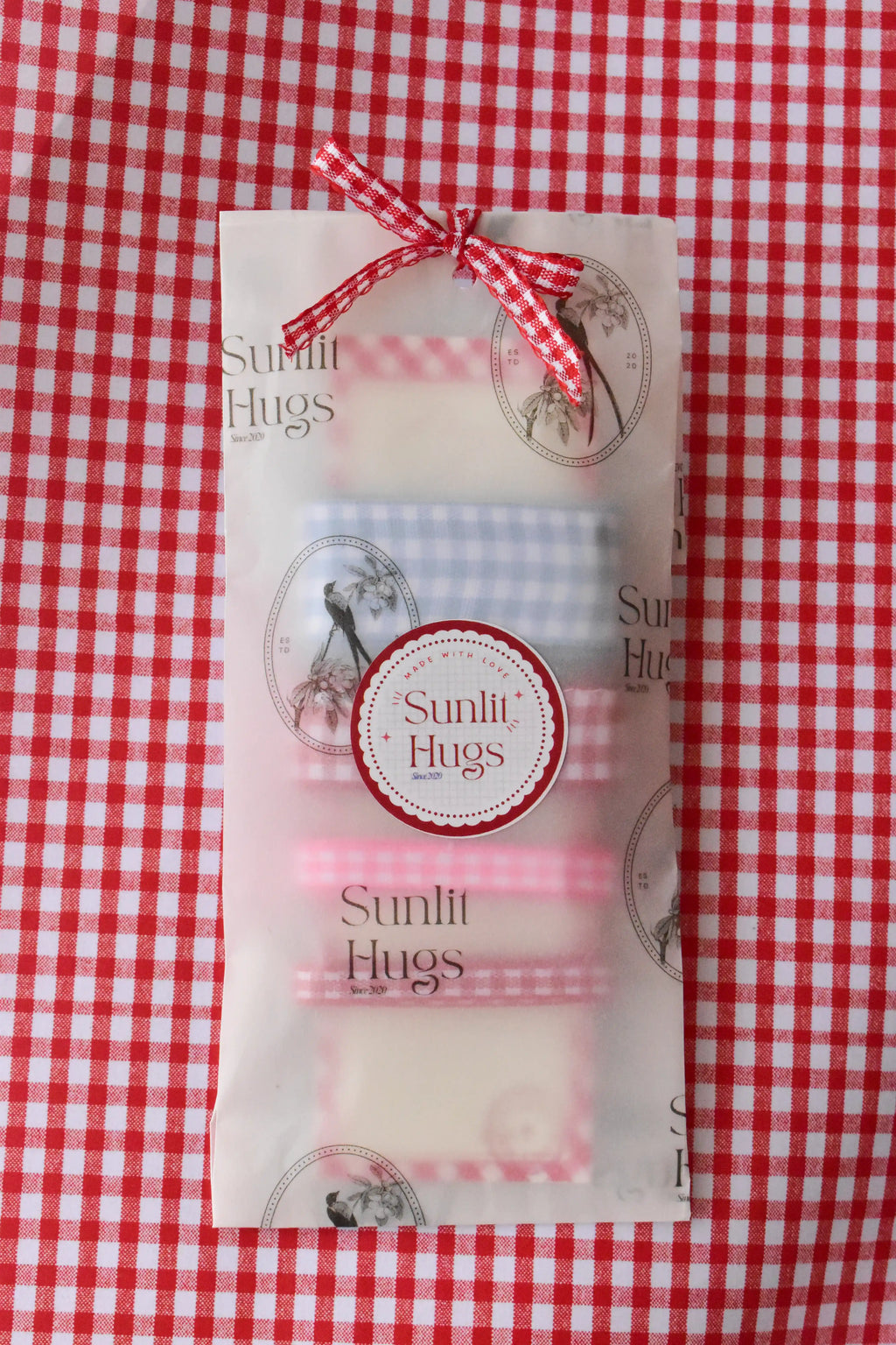 The Sky and Berries Ribbon Set beautifully wrapped in Sunlit Hugs branded vellum paper and tied with a red gingham ribbon bow.