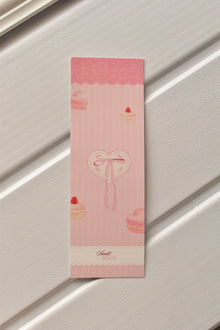This image shows a detailed, centered view of the Bow Bookmark front, highlighting the soft pastel pink colour and the charming macaron and heart illustration with a delicate bow.