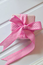 A top-down view of a small, wrapped gift. The Candy Stripes ribbon, with its pink and white diagonal pattern, is tied into a double bow, showcasing its use for gift wrapping.