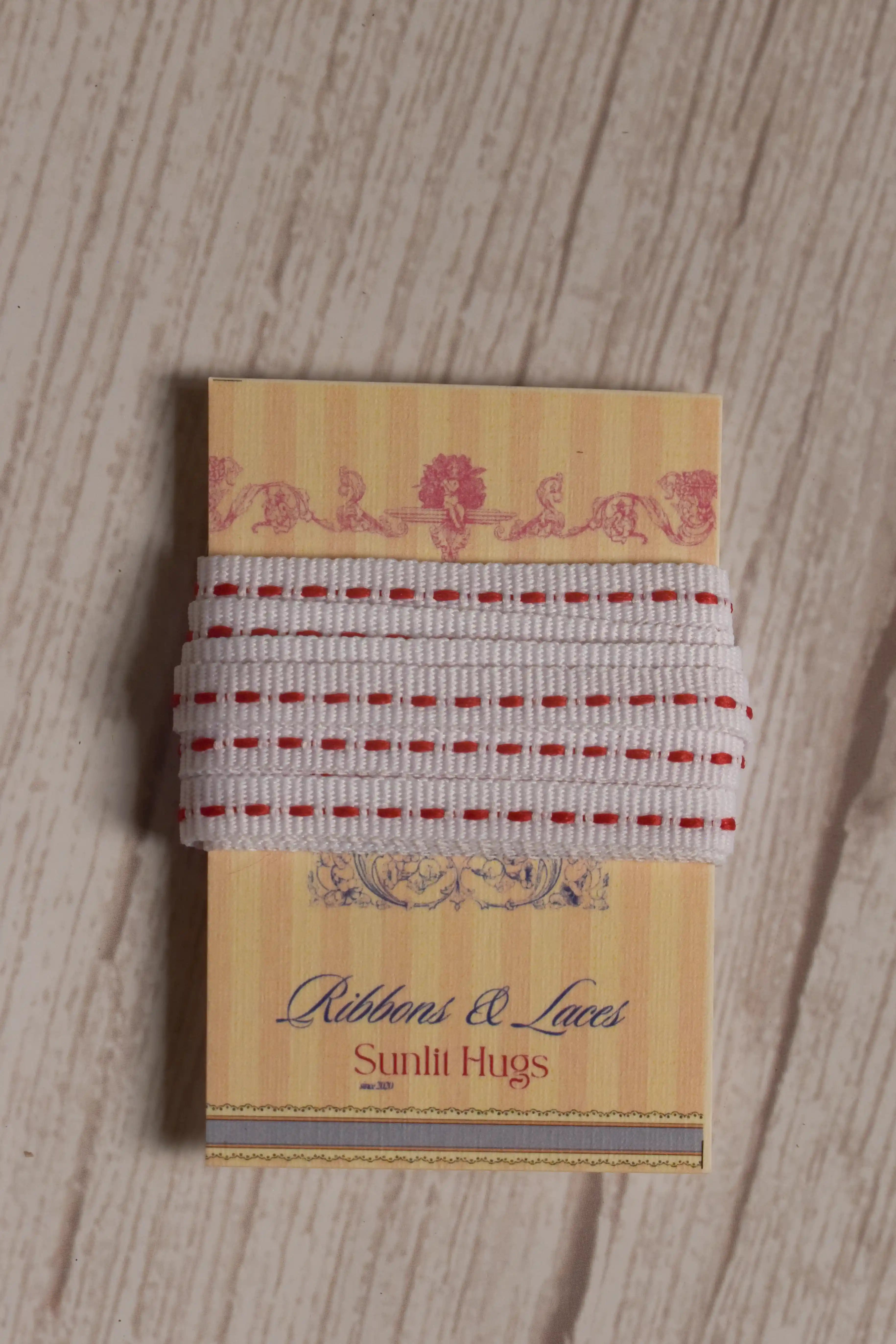 Candy Seam Narrow Ribbon displayed on a Sunlit Hugs ribbon card, showing its white base, red stitched detailing, and narrow 6 mm width.