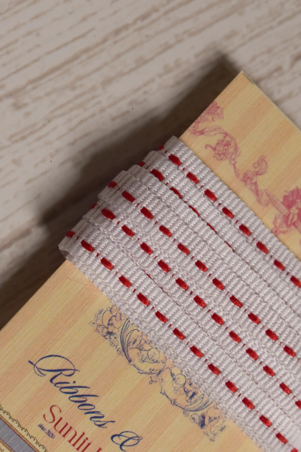 Close-up of Candy Seam Narrow Ribbon with a white woven look and red seam-style detailing, shown wrapped around a Sunlit Hugs ribbon card.