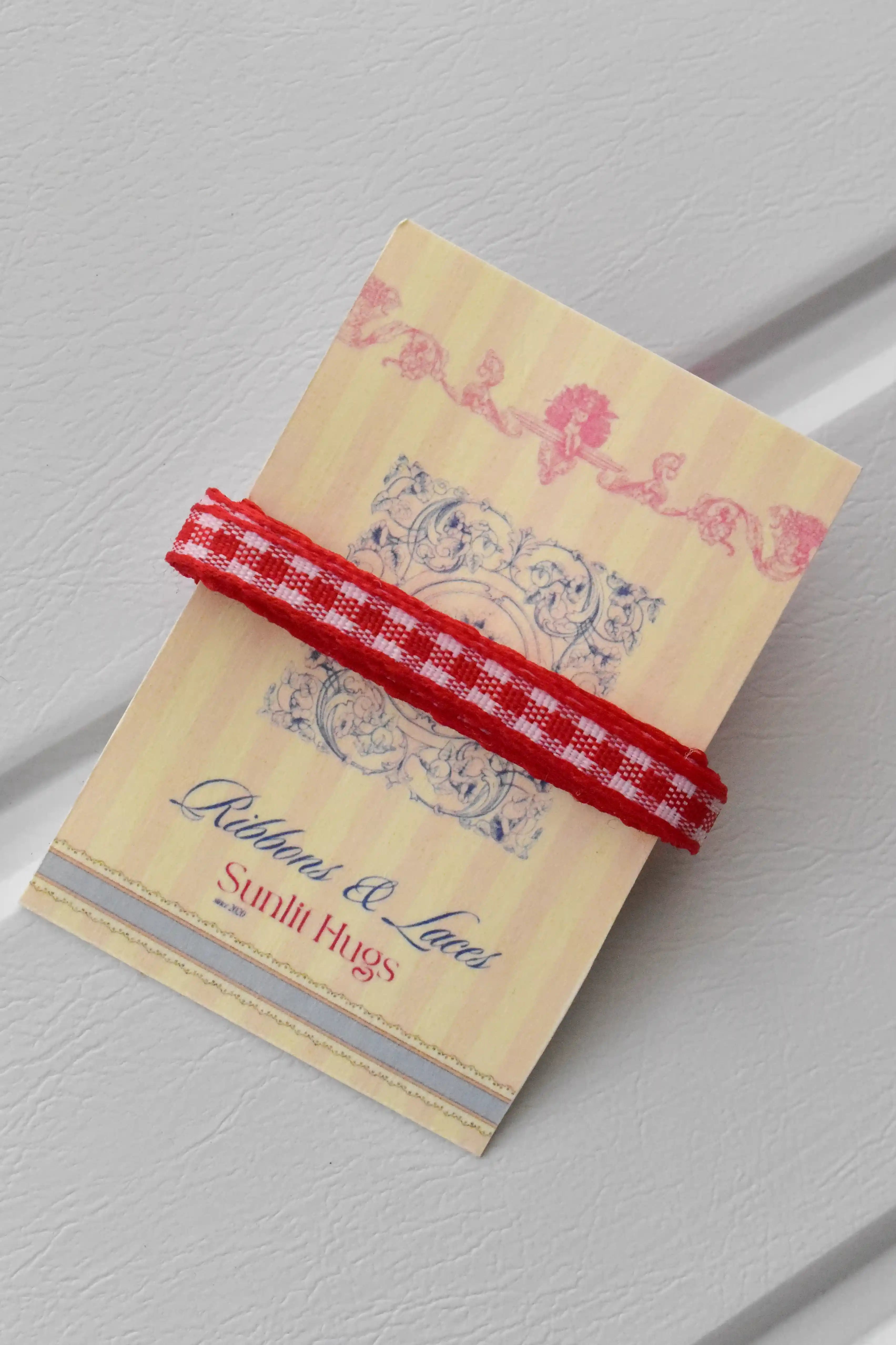 This close-up shows a swatch of the Cherry Picnic narrow ribbon, highlighting its classic red and white checkered pattern and woven texture, neatly wrapped around a "Sunlit Hugs" brand tag.