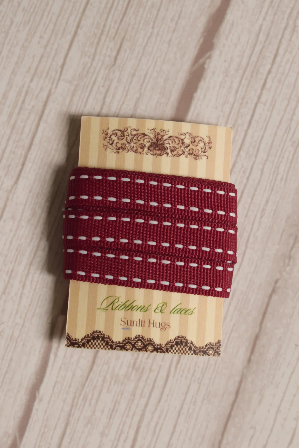 Cherry Stitches Ribbon wrapped around a printed Sunlit Hugs ribbon card, showing its 10 mm width, red woven finish, and white stitched design.