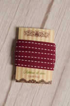 Cherry Stitches Ribbon wrapped around a printed Sunlit Hugs ribbon card, showing its 10 mm width, red woven finish, and white stitched design.
