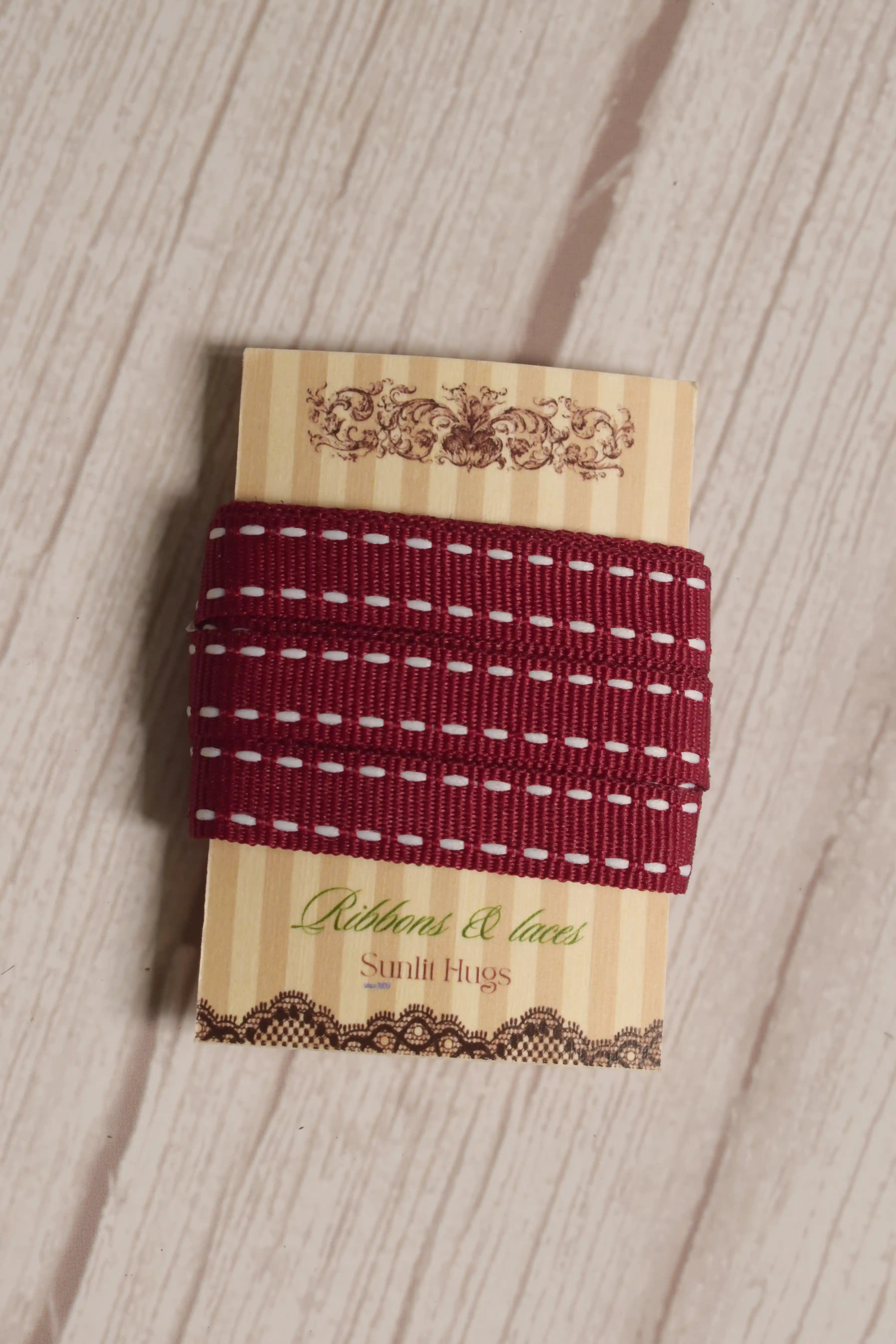 Cherry Stitches Ribbon wrapped around a printed Sunlit Hugs ribbon card, showing its 10 mm width, red woven finish, and white stitched design.