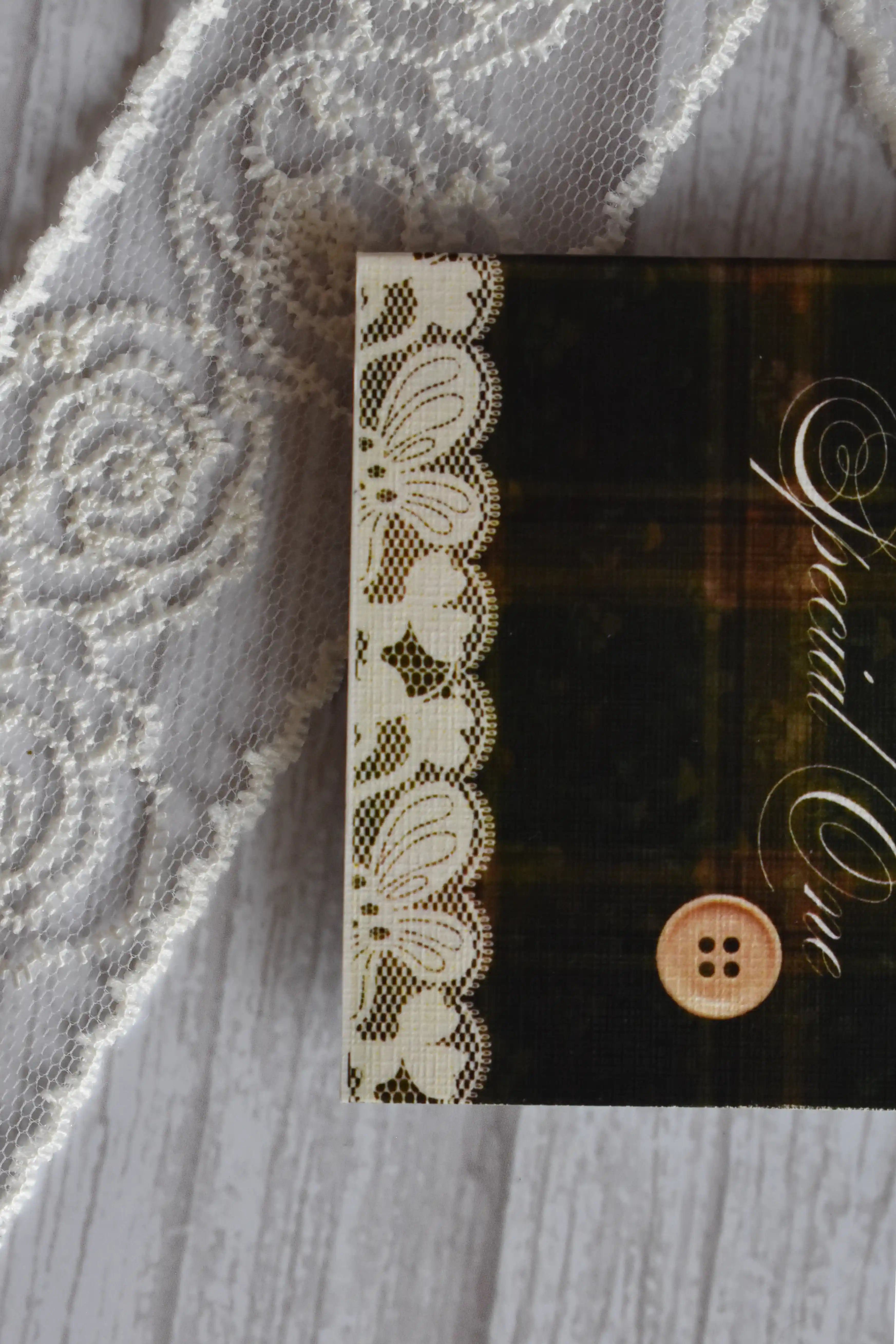 Macro close-up of the Sunlit Hugs Vintage Plaid Congratulations Greeting Card focusing on the printed white lace edge and vintage button detail against the dark plaid background.