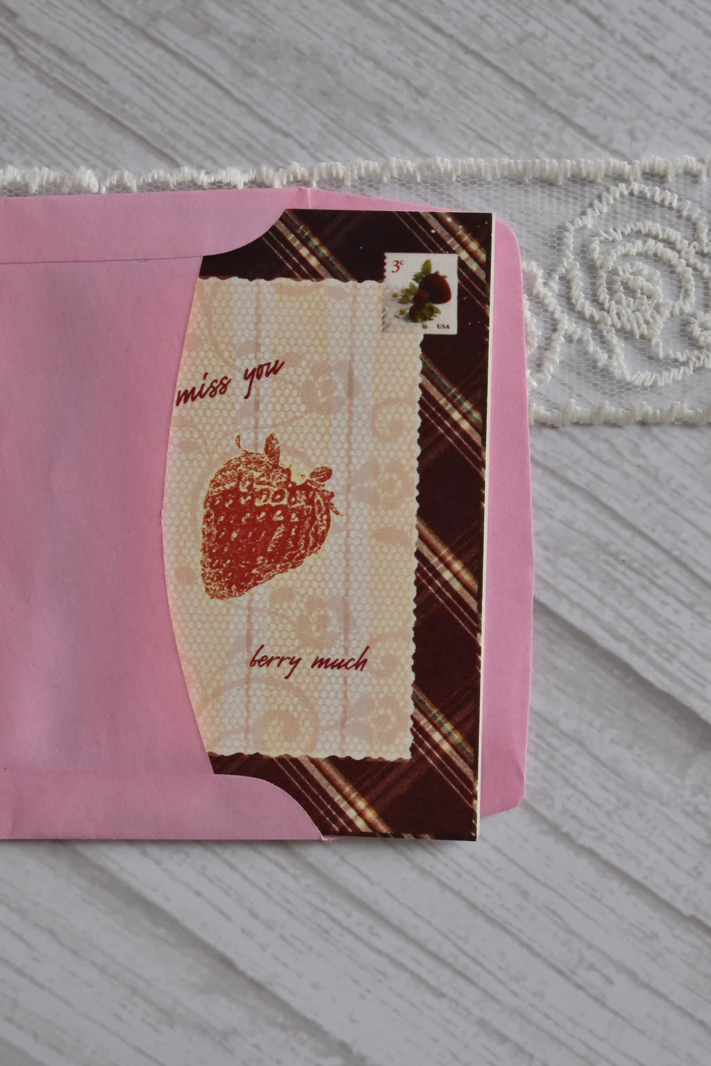 Close-up of the Sunlit Hugs I Miss You Berry Much Greeting Card inside a pink envelope, focusing on the strawberry illustration, text, and faux vintage stamp.