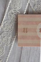 Macro close-up of the back of the Sunlit Hugs Life Feels Kinder With You Greeting Card focusing on the pink stripes, logo, and a piece of white vintage lace.