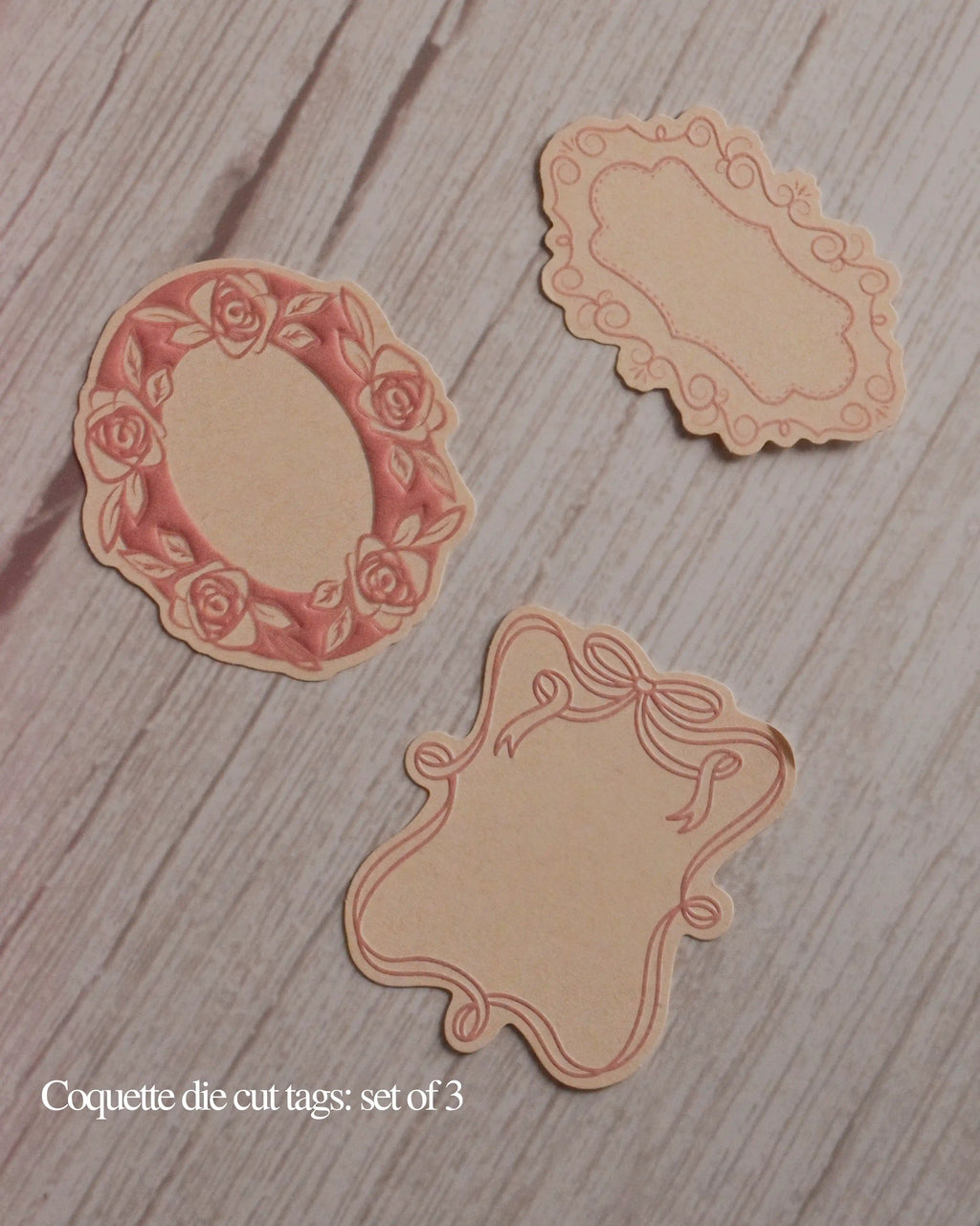 Three decorative die-cut tags on a wooden surface with 'Coquette die cut tags: set of 3' text.