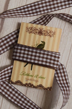 Cortado Checks Ribbon shown with loose brown and white checked ribbon strands around the product card, suitable for craft projects, packaging, scrapbooking, and decorative bows.