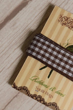 Close-up of Cortado Checks Ribbon wrapped around a printed Sunlit Hugs ribbon card, highlighting its brown and white checked design and 16 mm width.