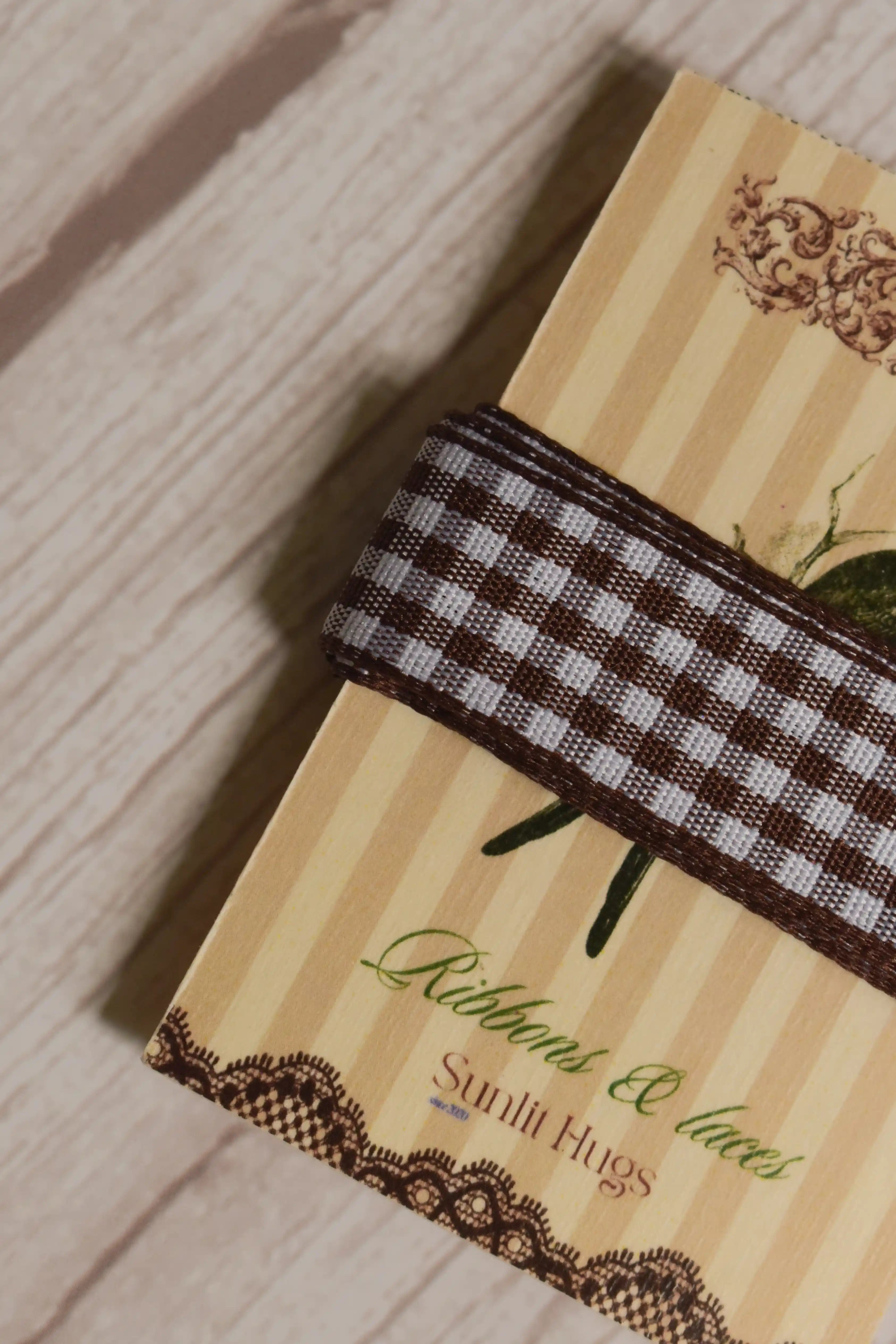 Close-up of Cortado Checks Ribbon wrapped around a printed Sunlit Hugs ribbon card, highlighting its brown and white checked design and 16 mm width.