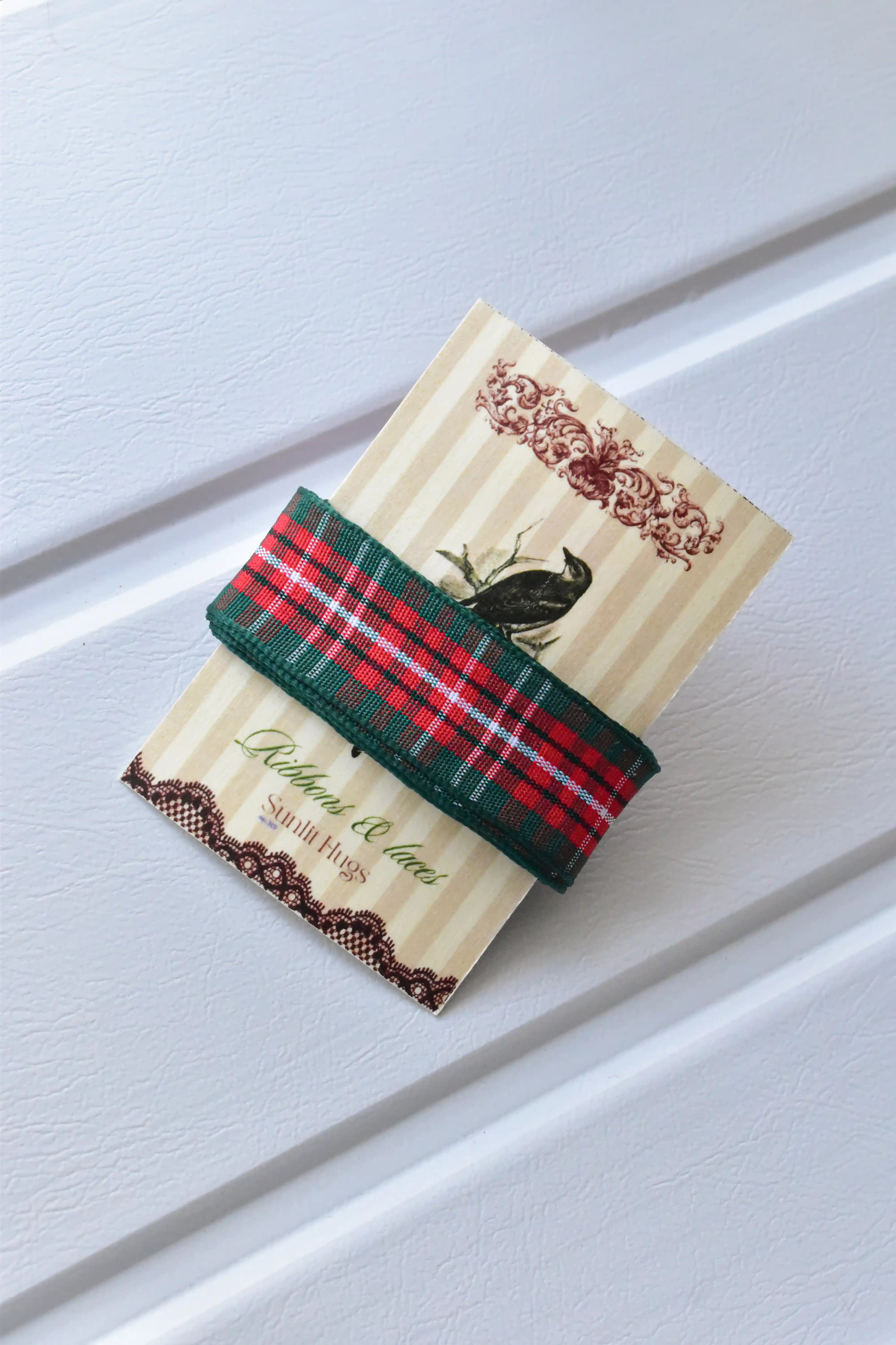 This detailed view showcases the Cranberry Trail ribbon, highlighting its classic red and green plaid pattern and woven texture, neatly presented on a "Sunlit Hugs" brand tag.

