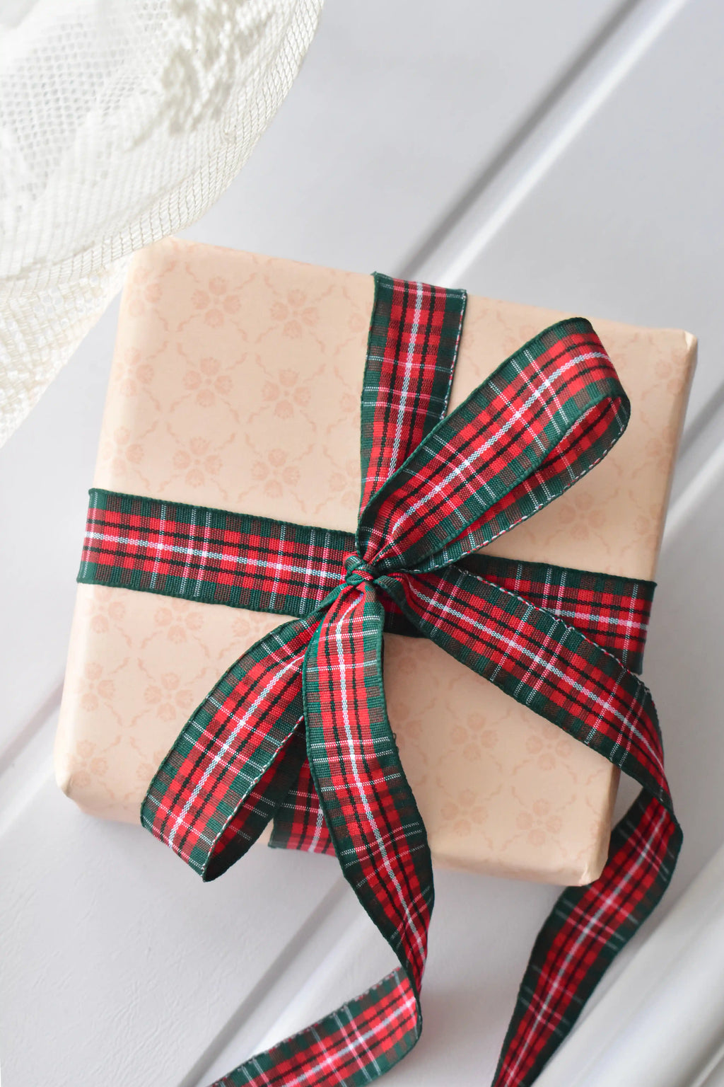 This image shows a beautifully wrapped gift box, featuring the Cranberry Trail ribbon with its red and green plaid pattern, tied into an elegant bow, demonstrating its festive use for gift presentation.