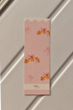 This image shows a detailed, centered view of the Croissant Bookmark front, highlighting the soft pastel pink colour and the charming croissant illustration.