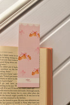 This warm shot demonstrates the bookmark in action, showing the croissant illustration and pastel pink colour tucked inside a book, perfect for marking a cosy reading moment.