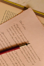 Close-up of the vintage brown letter sheet with flowing calligraphy script printed on it, with a red fountain pen resting on the message.