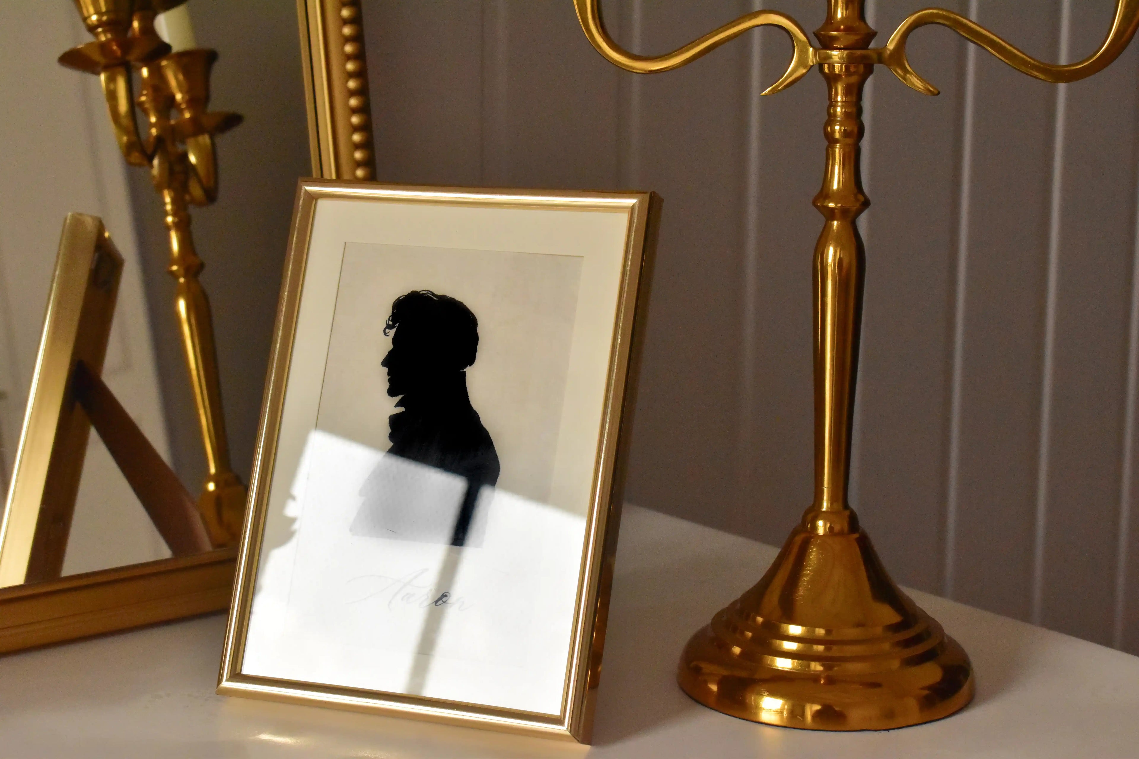 This angled image focuses on the texture and reflection on the golden frame, showing the black silhouette portrait beautifully displayed next to a gold candelabra.