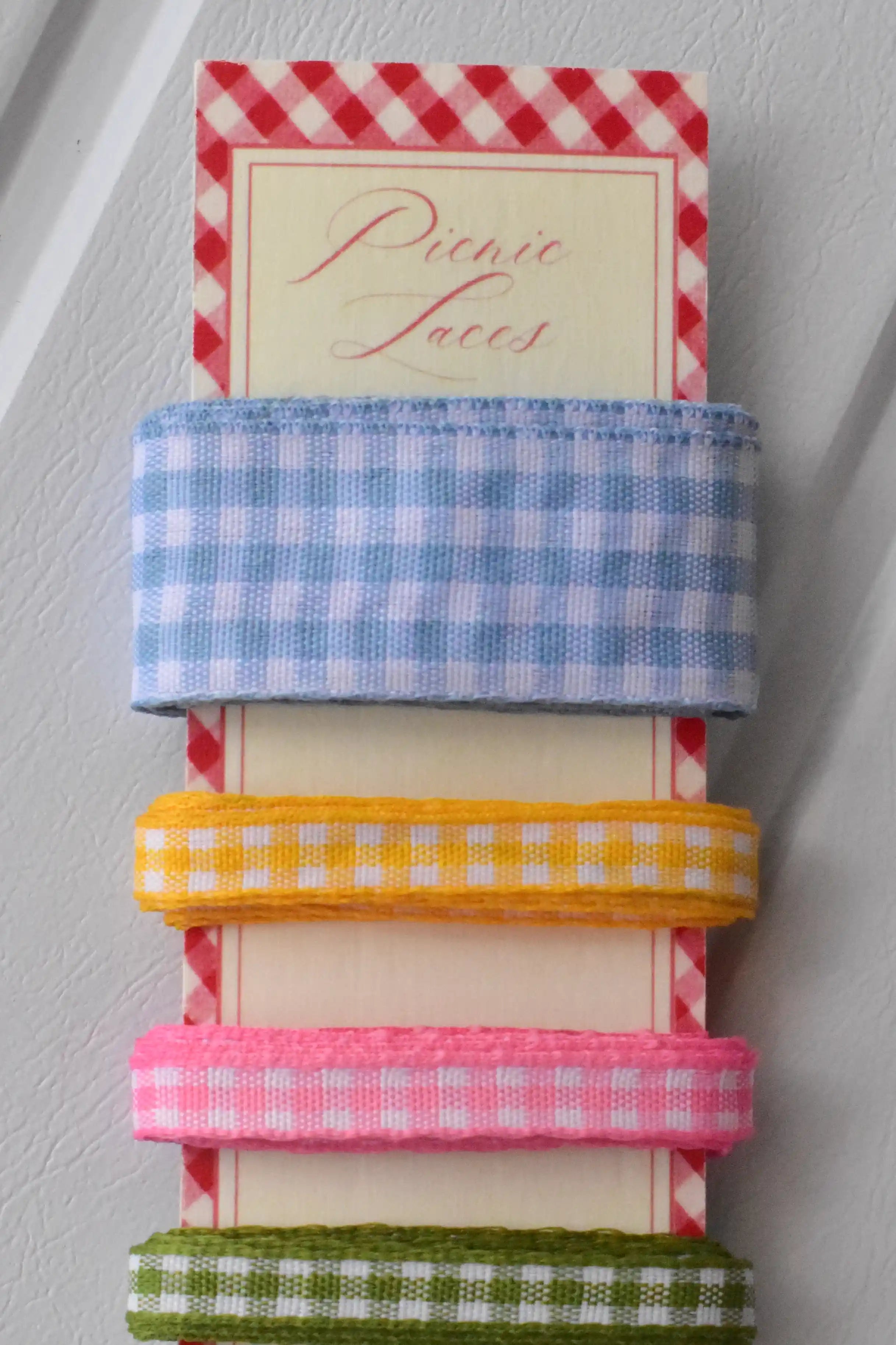 Close-up stack of the top three narrow gingham ribbons in blue, yellow, and pink, showing the texture of the weave.
