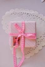 A small, pink striped gift box tied with a narrow pink and white gingham ribbon (2 Metres) bow.