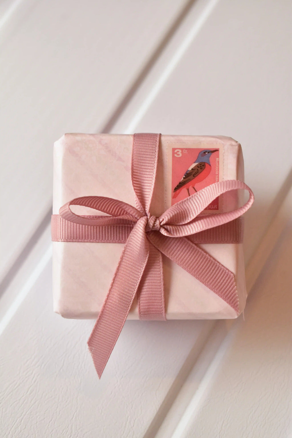 This image shows a beautifully wrapped gift box, featuring the Rustic Blush ribbon tied into a lovely bow. The ribbon's elegant rose gold colour adds a sophisticated touch to the present, complemented by a charming vintage-style stamp.