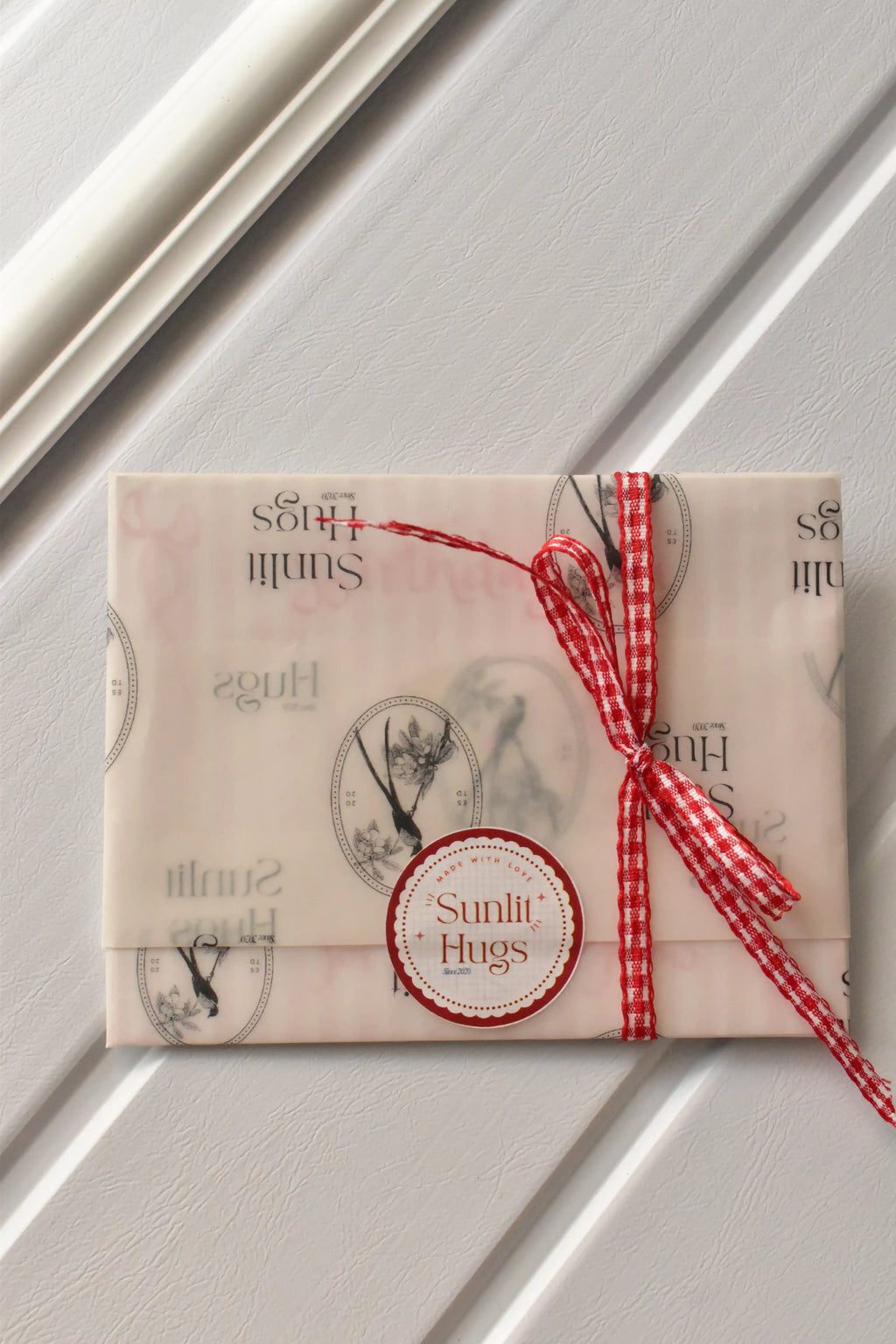 This view assures customers of the thoughtful gift presentation, showing the postcard set wrapped in Sunlit Hugs vellum paper and secured with a sweet gingham ribbon.