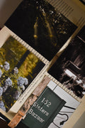 Flat lay collage of the Vintage Landour Photo Print Set resting on the pages of an open book, showcasing four 3x4 inch fine art photography prints: a sunlit forest canopy, blooming blue hydrangeas, a moody vintage window, and a classic "152 Sisters Bazaar" sign.