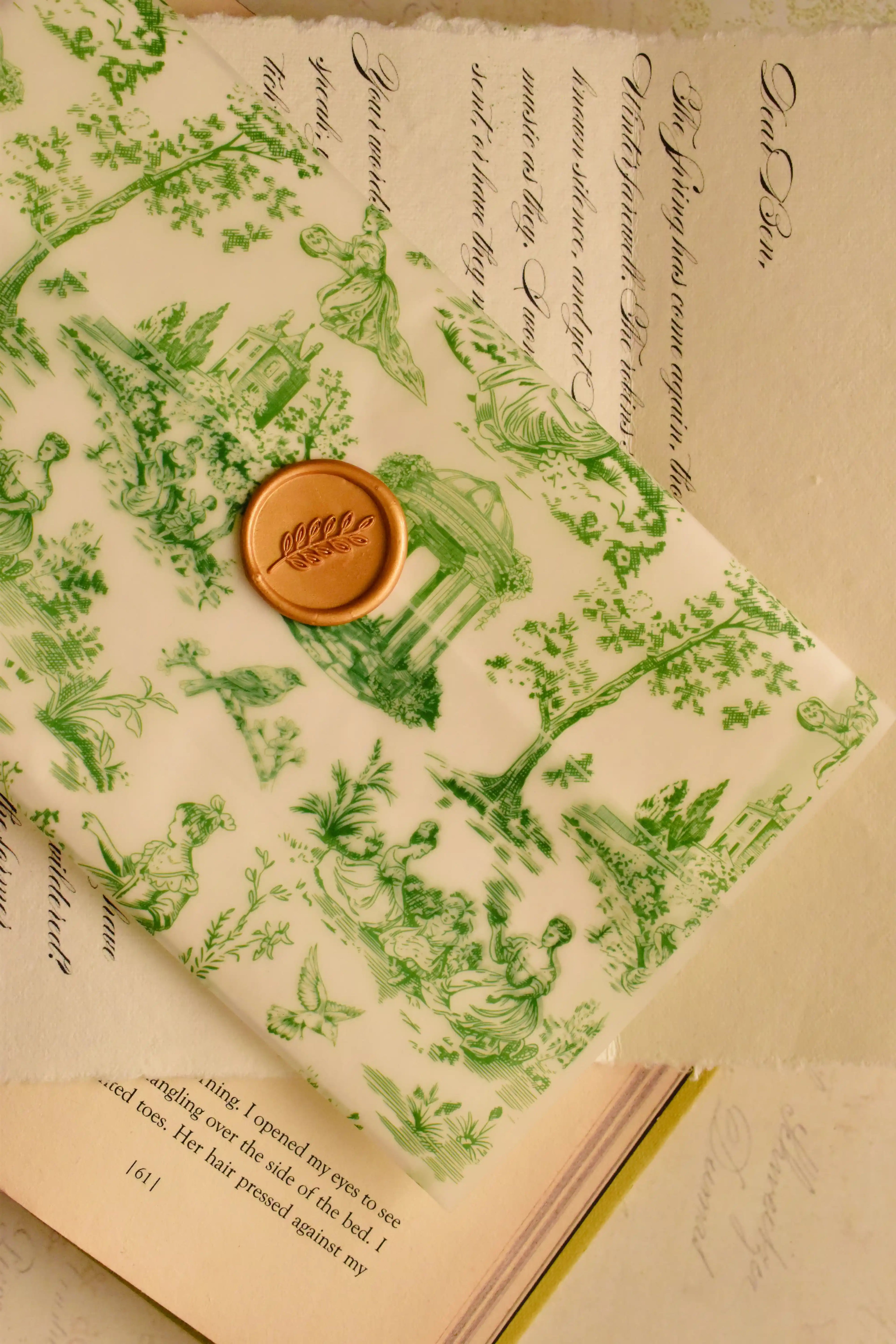  This image beautifully displays the green toile vellum envelope sealed with the golden wax stamp, resting atop a book and showcasing the whimsical, antique charm of the letter.