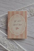 Front cover of the Sunlit Hugs Life Feels Kinder With You Greeting Card showing light pink stripes, a delicate white lace doily border, and romantic calligraphy.