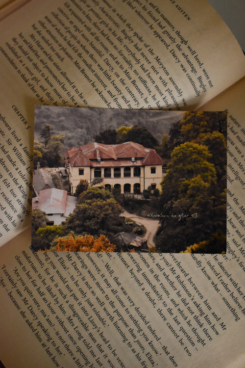 Front view of the 'Khwabon Ka Ghar' Barlowganj Photo Print by Anneshwa Paul displayed on an open book, capturing the dark academia aesthetic of a majestic mountain house of dreams.
