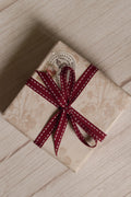 A vintage-style gift parcel tied with Cherry Stitches Ribbon, showing the cherry red ribbon with white stitched detail styled as a decorative bow.
