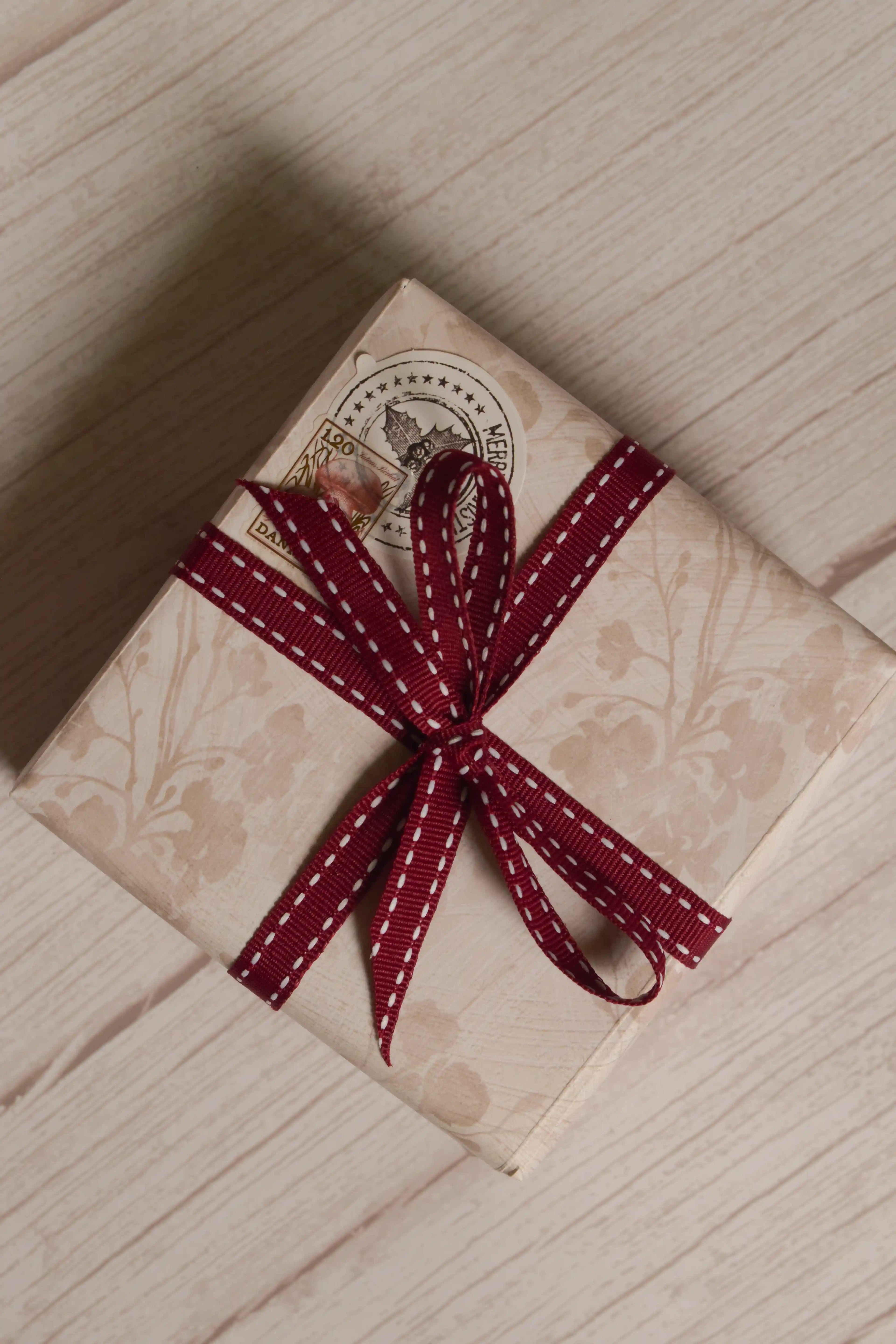 A vintage-style gift parcel tied with Cherry Stitches Ribbon, showing the cherry red ribbon with white stitched detail styled as a decorative bow.