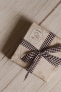 A vintage-style gift parcel tied with Cortado Checks Ribbon, showing the brown and white checked ribbon styled as a bow for warm and thoughtful packaging.