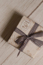 A vintage-style gift parcel tied with Cortado Checks Ribbon, showing the brown and white checked ribbon styled as a bow for warm and thoughtful packaging.